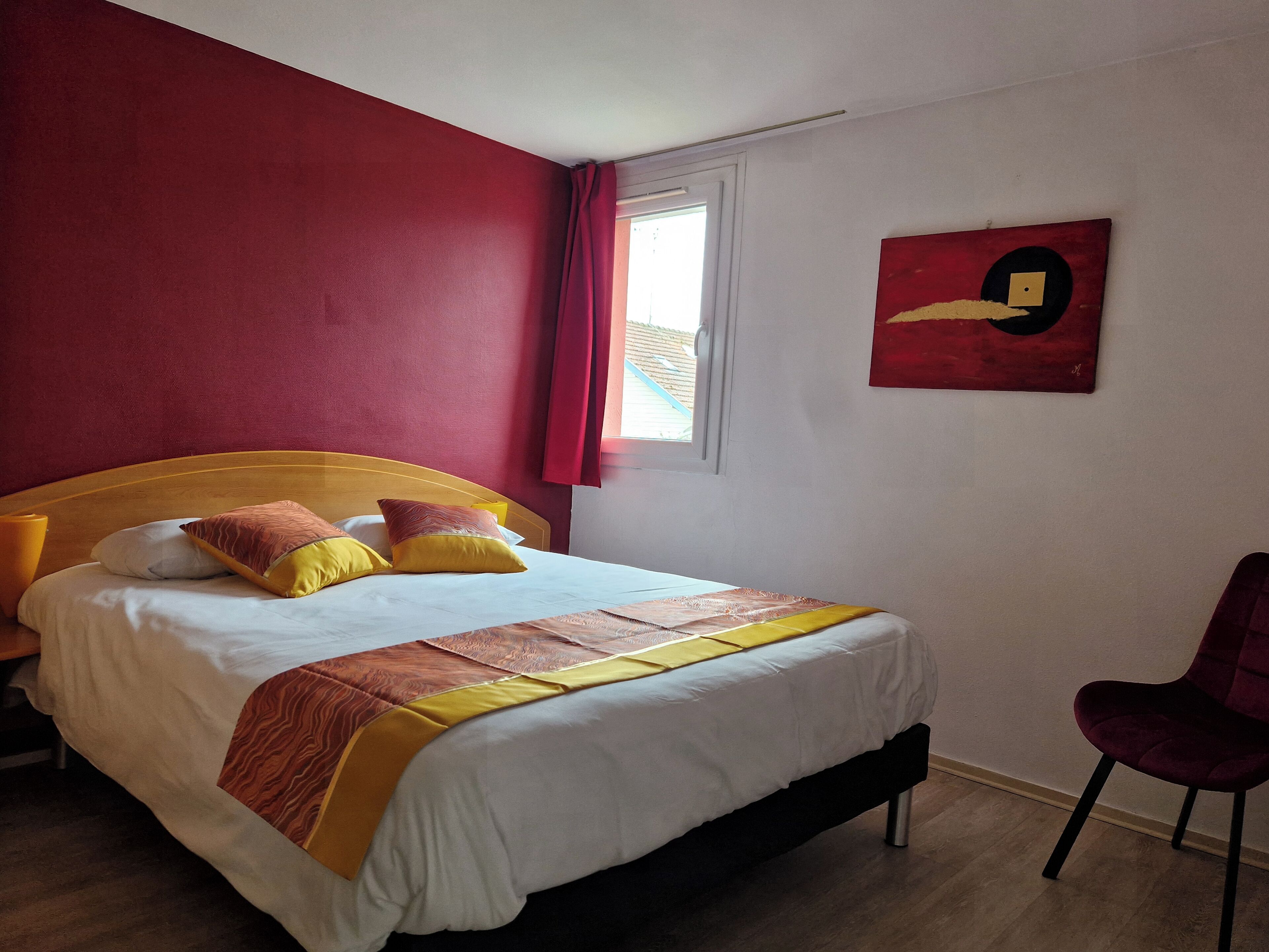 A hotel room with a bed, a chair, a window, and a painting on the wall.