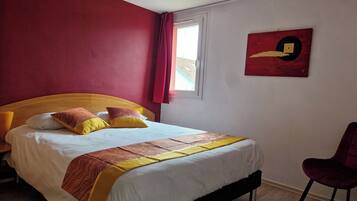 A hotel room with a bed, a chair, a window, and a painting on the wall.