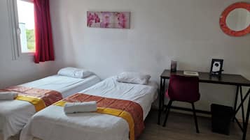 A room with two single beds, a desk, a chair, a mirror, and a window with curtains.