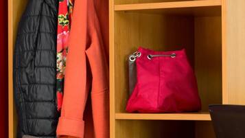 A wooden wardrobe with a hanging rack, a red handbag, and a silver suitcase.