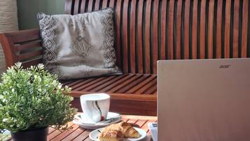 Ein Holztisch mit einem Laptop, einer Tasse, einem Untertasse, einem Teller mit Gebäck und einer Topfpflanze.