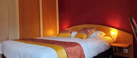 Habitación de hotel con una cama grande, cabecero de madera y una pared de acento roja.