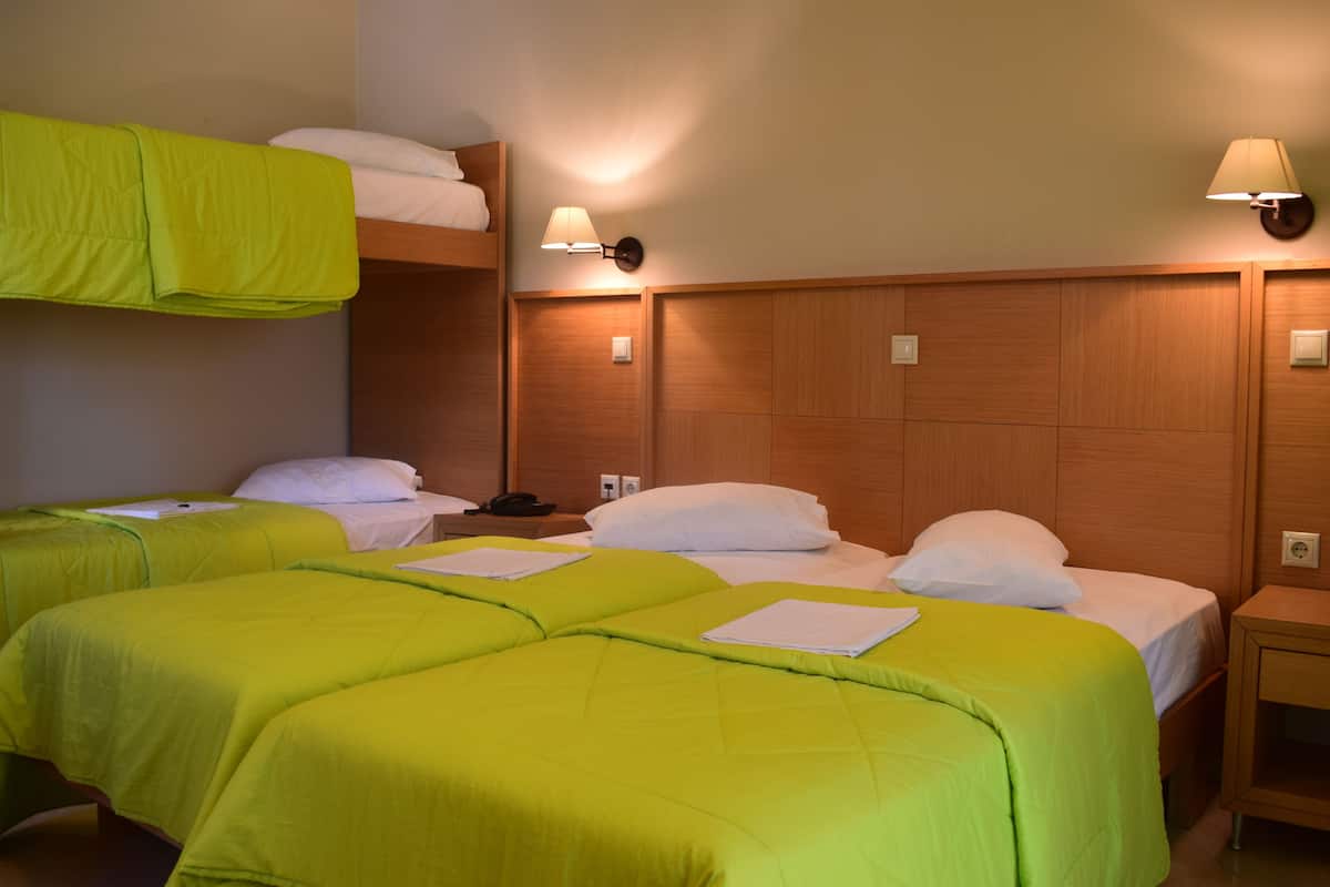 A hotel room with two single beds, each with a green bedspread and white pillows. There are two bedside tables with lamps, and a wooden headboard.