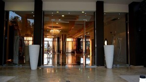 Un moderno vestíbulo de hotel con entrada de vidrio, grandes macetas blancas y una araña.