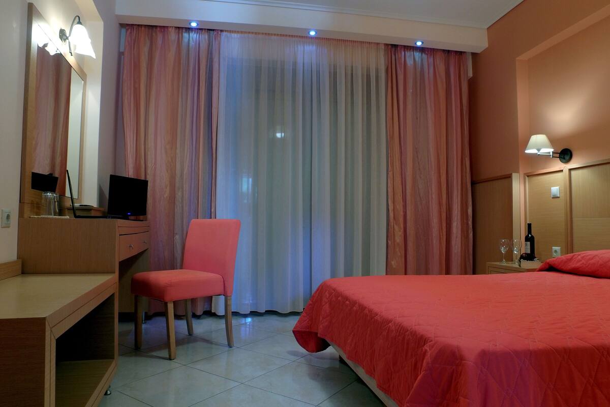 A hotel room with a bed, a desk with a computer, a chair, and a window with curtains.
