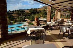 Un espace de restauration en plein air, avec des tables et des chaises, offrant une vue sur une piscine et un paysage vallonné.