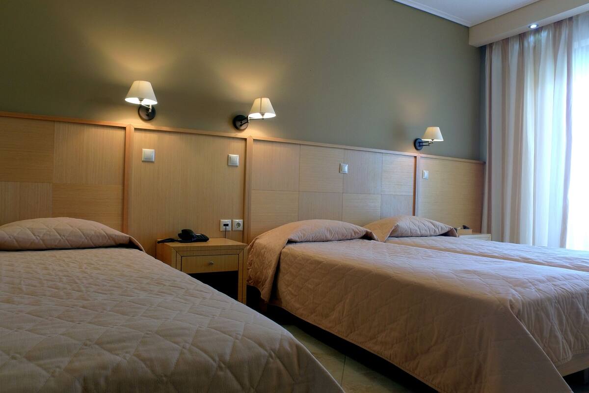 A hotel room with two beds, each with a headboard, a bedside table, and a lamp.