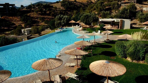 Una piscina con sillas de descanso y sombrillas, rodeada de vegetación y colinas.