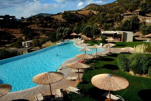 A swimming pool with lounge chairs and umbrellas, surrounded by greenery and hills. - Evia Hotel & Suites (Karystos)