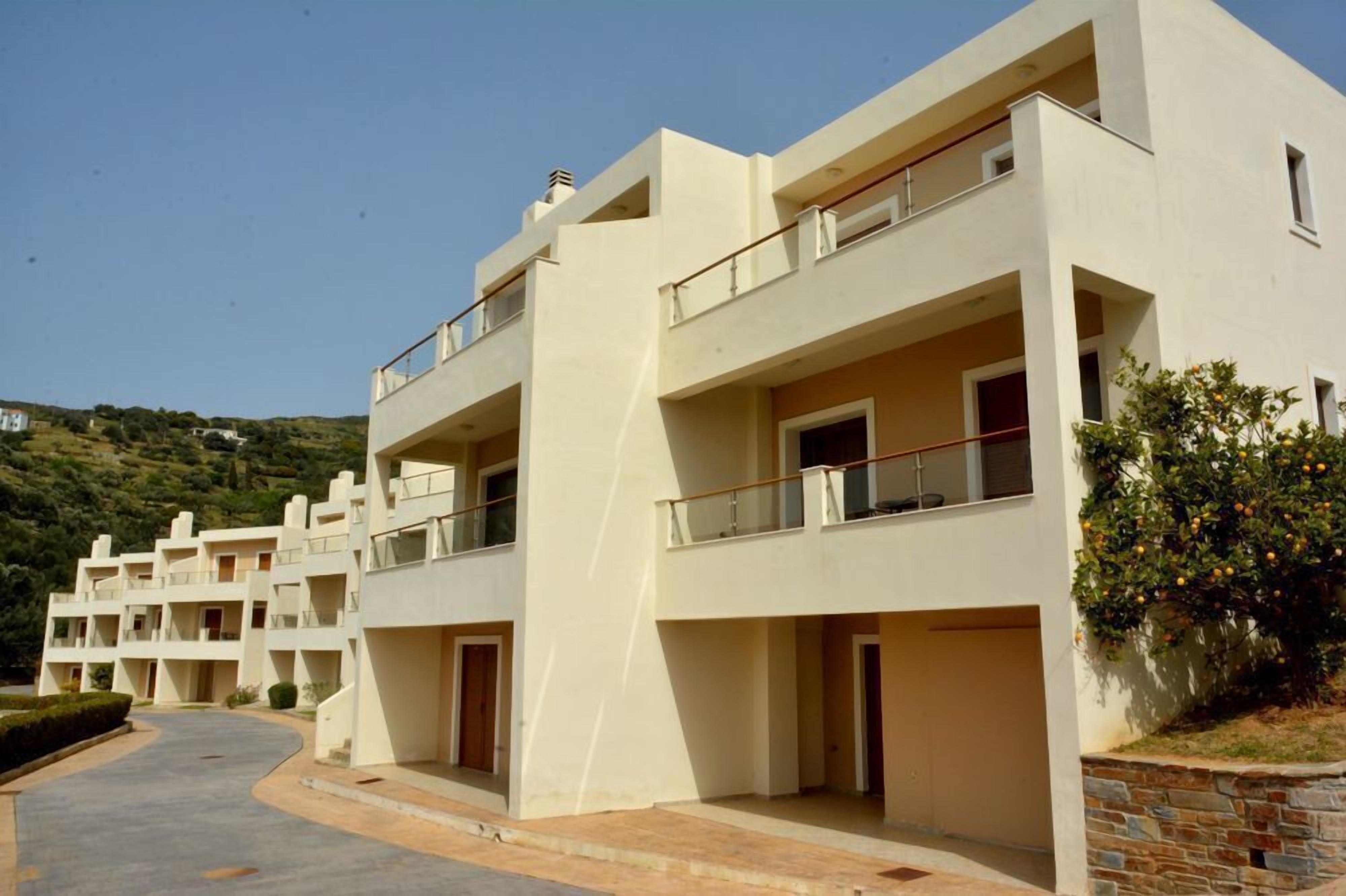 A modern multi-story residential building with balconies, a paved driveway, and a landscaped garden area.