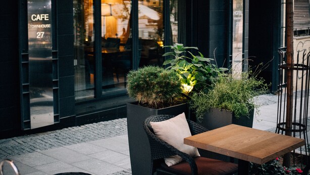 Un área de estar al aire libre con sillas de mimbre y una mesa de madera, una planta en maceta y luces colgantes.
