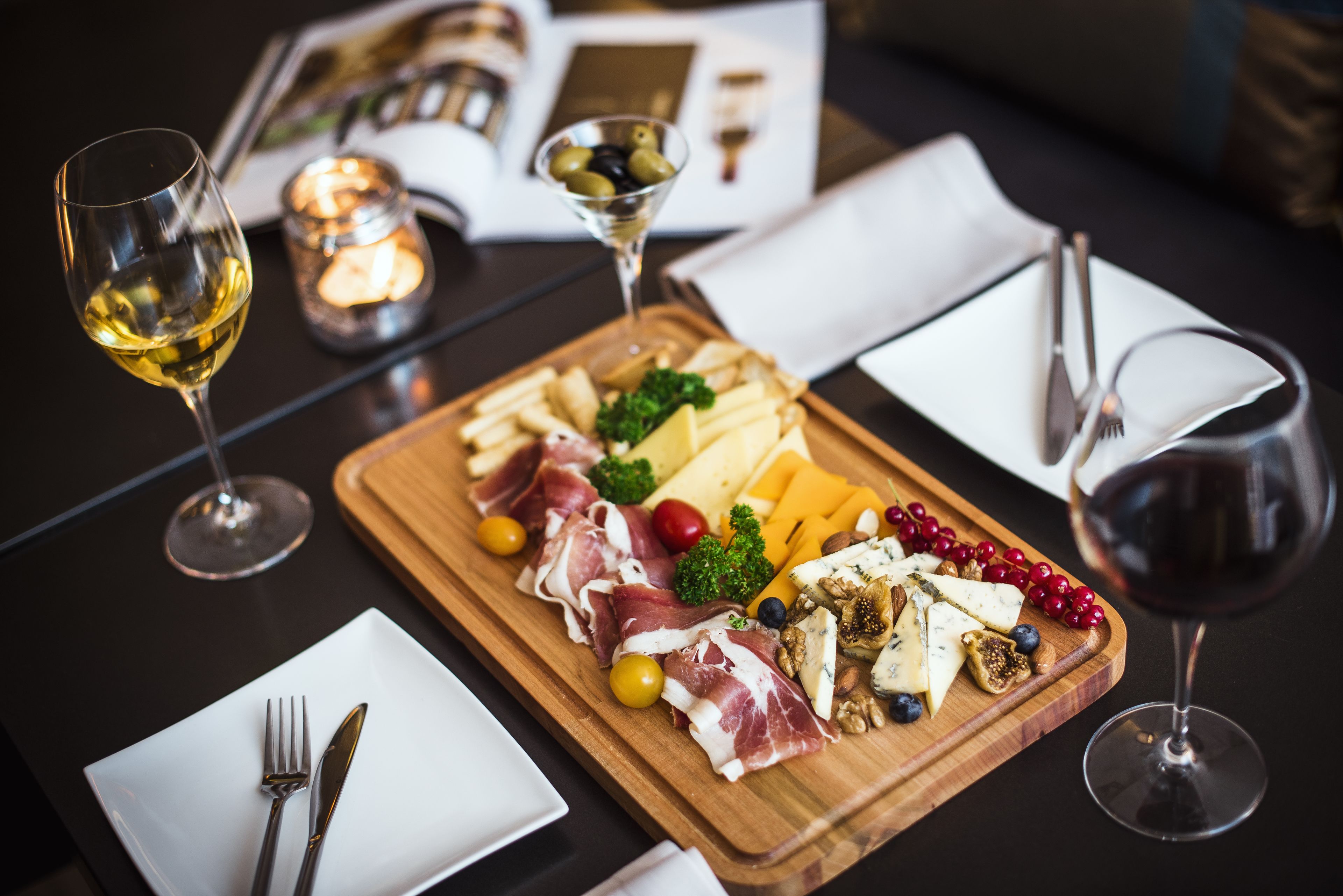 Une planche en bois garnie de différents fromages, de charcuteries et de fruits, accompagnée de verres à vin, le tout posé sur une table.