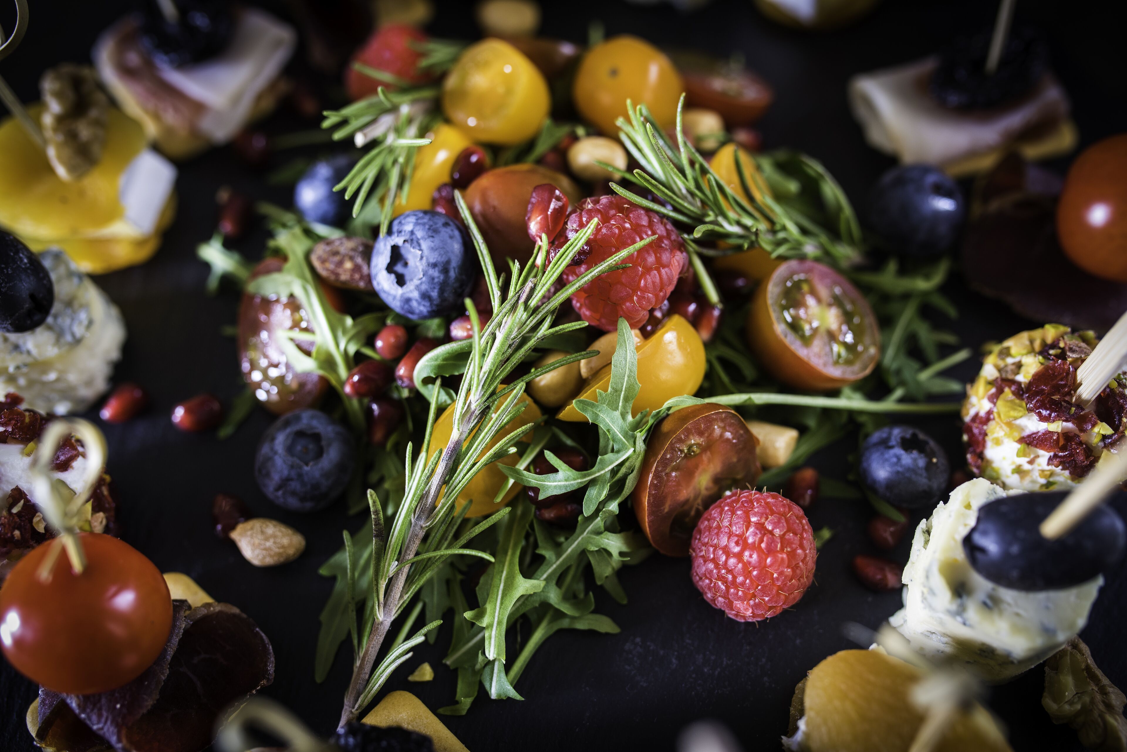 A variety of fruits and vegetables, including tomatoes, blueberries, and raspberries, arranged on a dark surface.