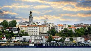 A waterfront cityscape with historic buildings, a prominent church tower, and a river in the foreground.