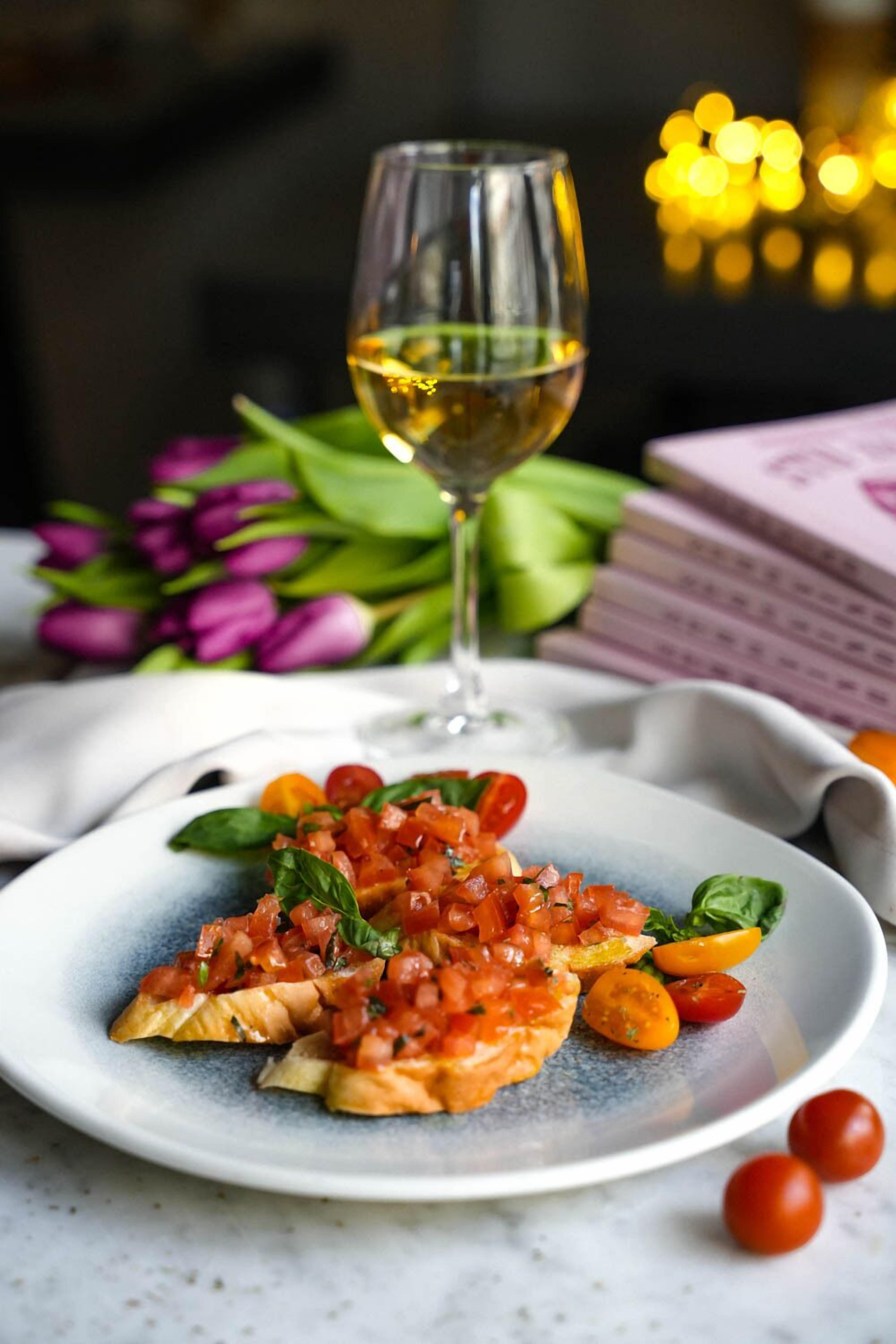 Un plato de comida con una copa de vino blanco, rodeado de flores y libros.