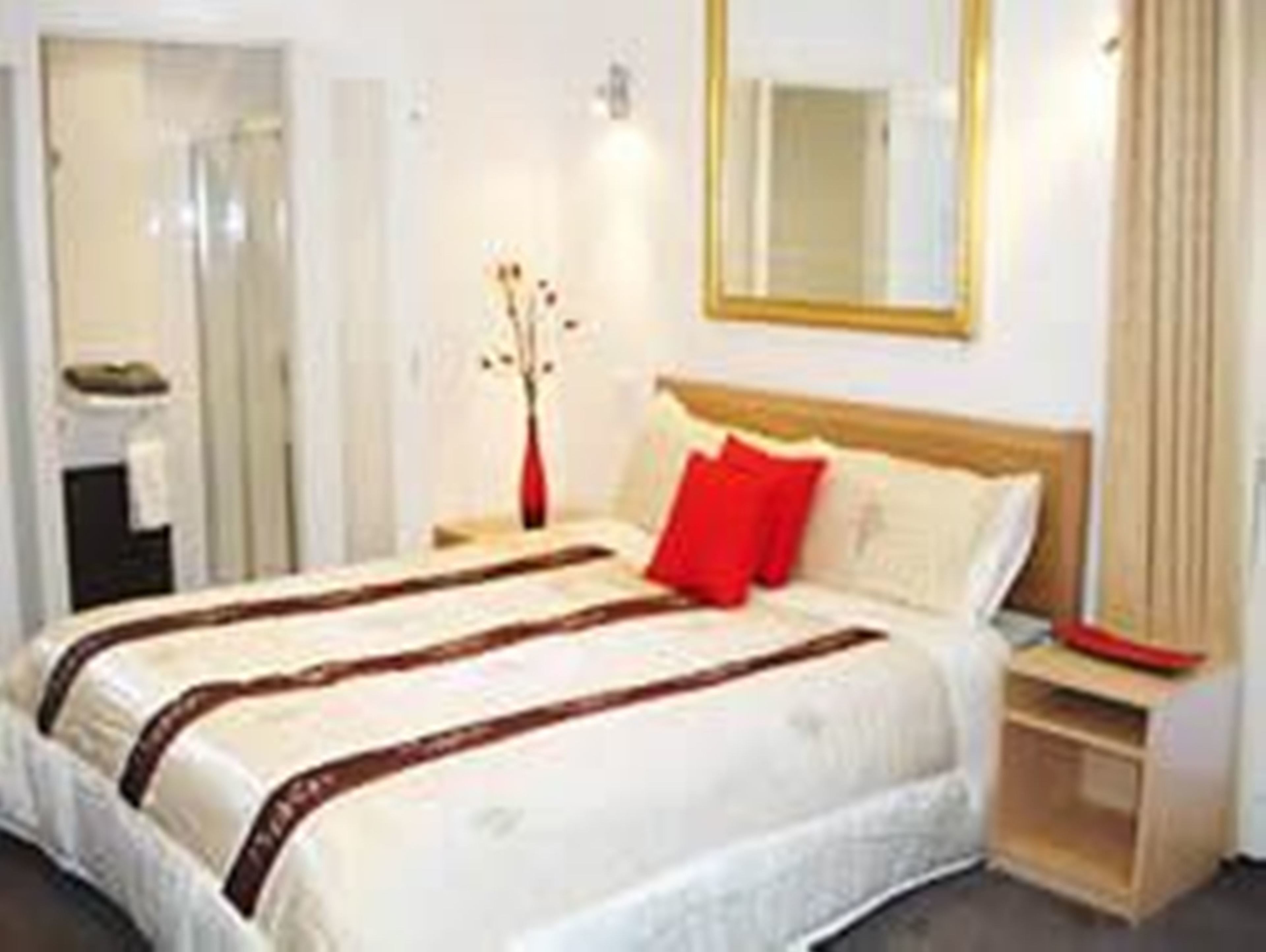 A hotel room with a bed, a nightstand, a mirror, and a vase with flowers.