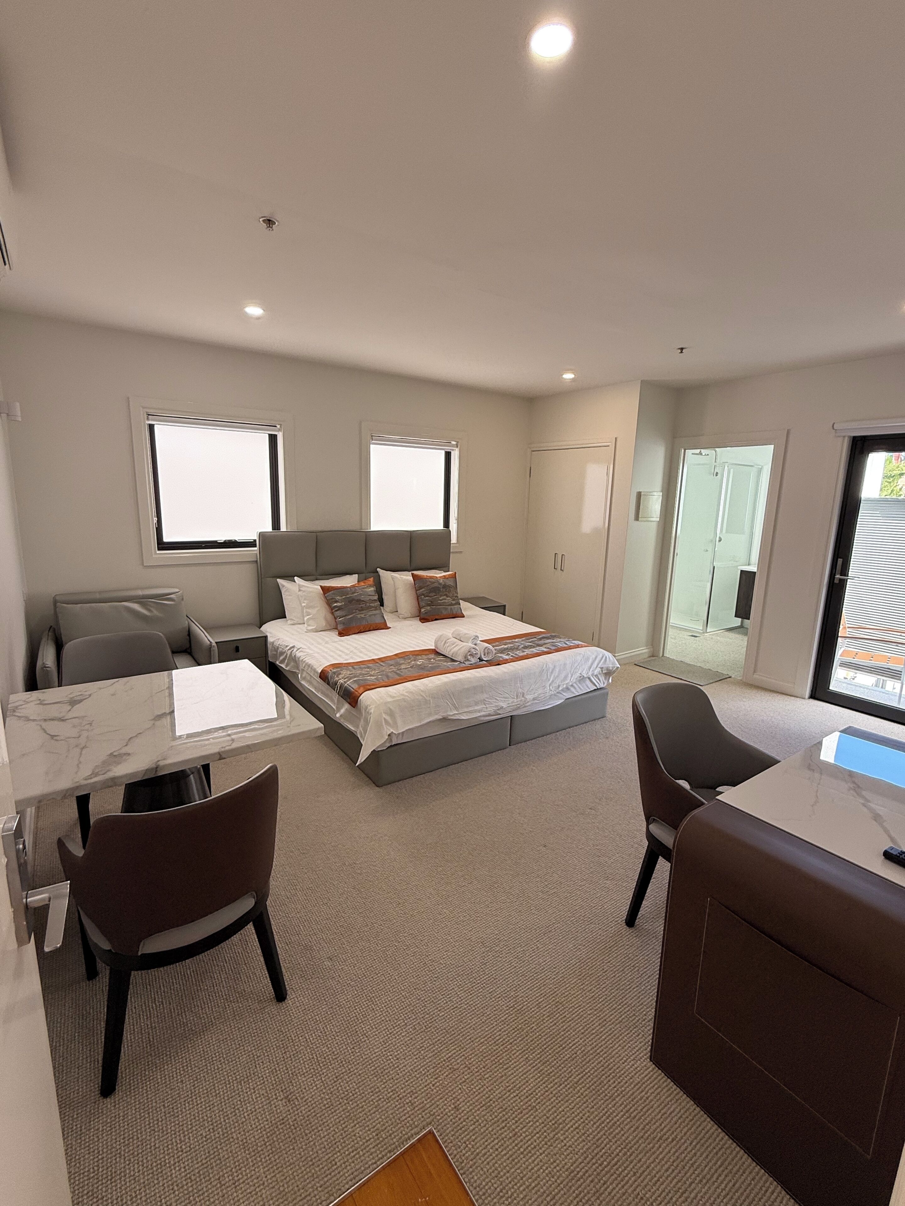 Une chambre d’hôtel avec un lit, un bureau, deux chaises, une fenêtre et une porte.