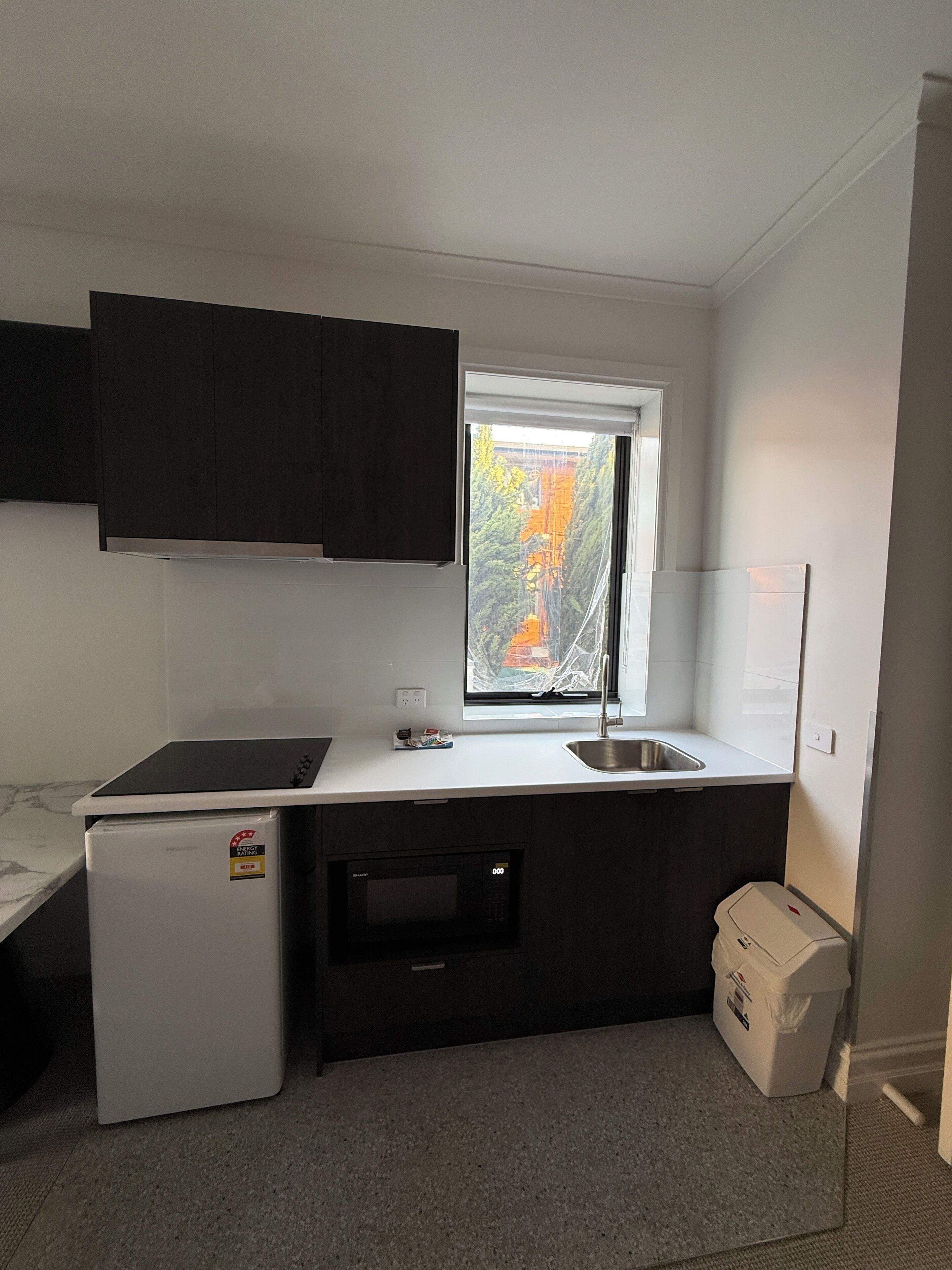 A compact kitchen with a built-in microwave, a small refrigerator, and a window with a view of trees.