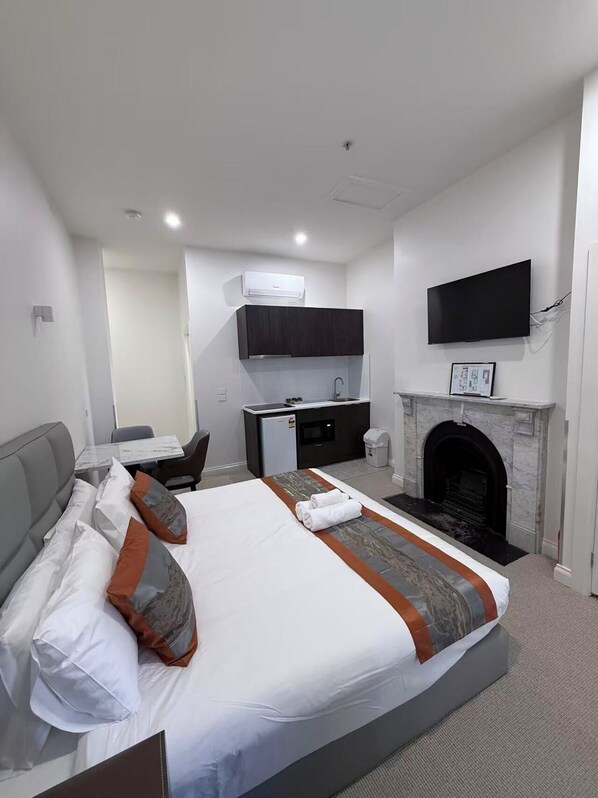 A modern hotel room with a large bed, a desk, a flat-screen TV, and a fireplace.