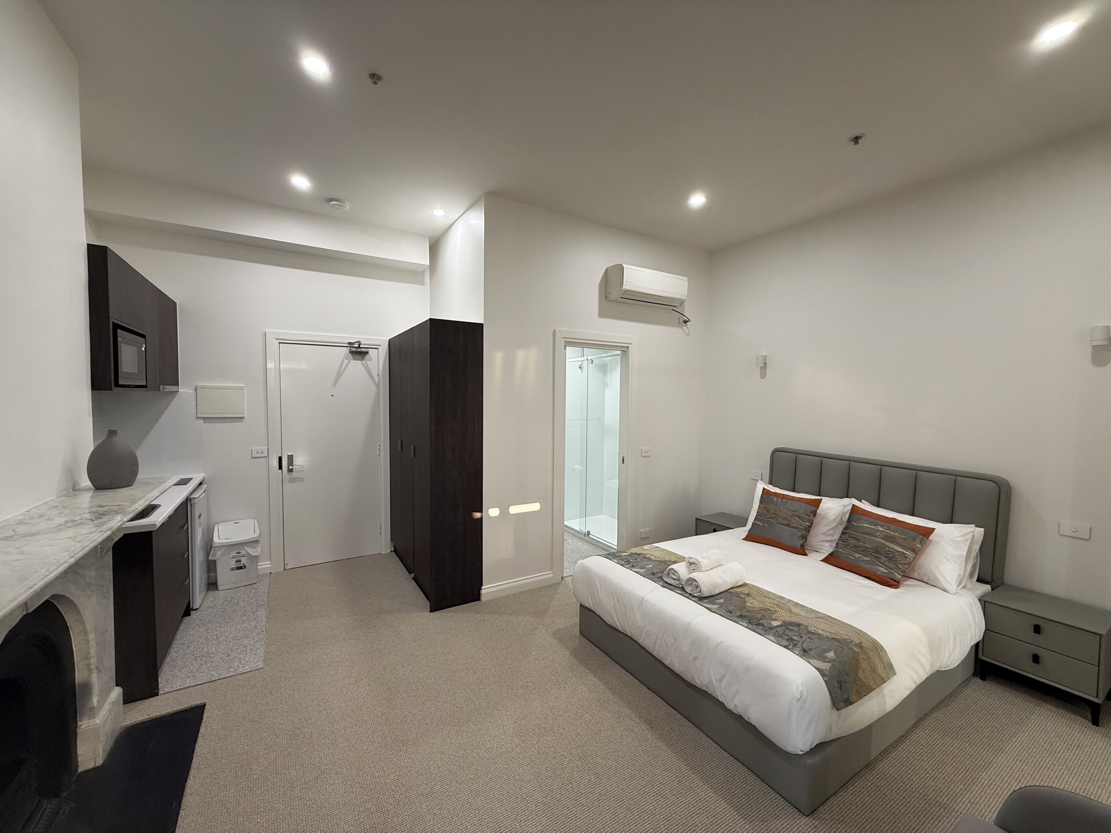 A modern bedroom with a large bed, bedside tables, a built-in wardrobe, a shower room, and a small desk area.