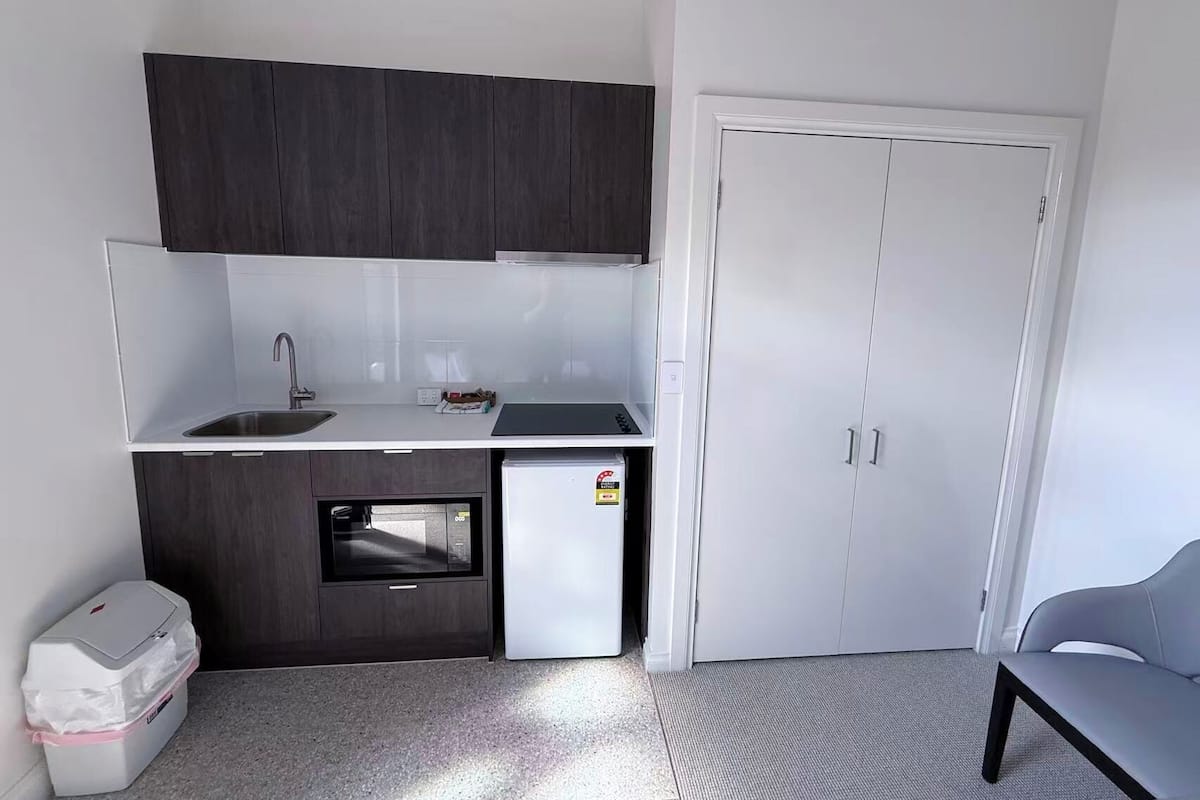A compact kitchen with a sink, a small refrigerator, dark cabinets, and a white door.