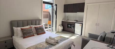 Una habitación de hotel moderna con cama, escritorio, silla, kitchenette y armario.