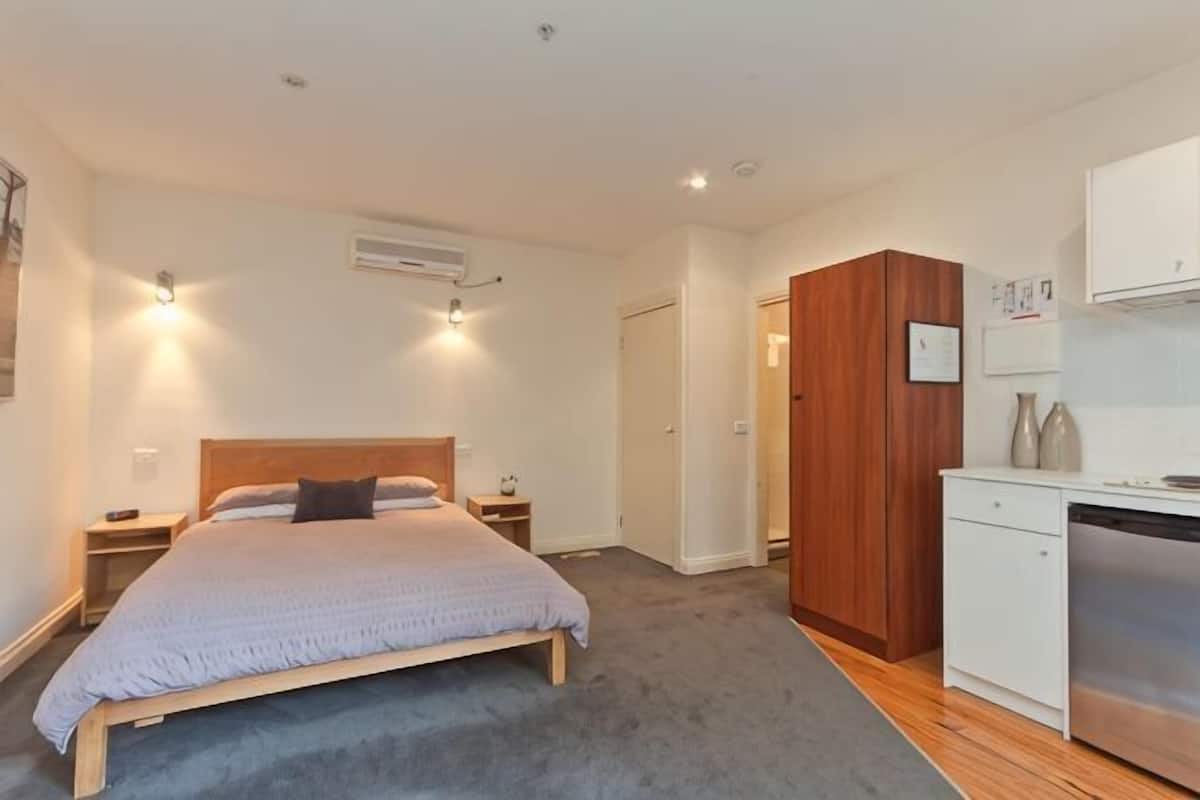 A bedroom with a bed, bedside tables, a wooden wardrobe, a white cabinet, and a built-in dishwasher.
