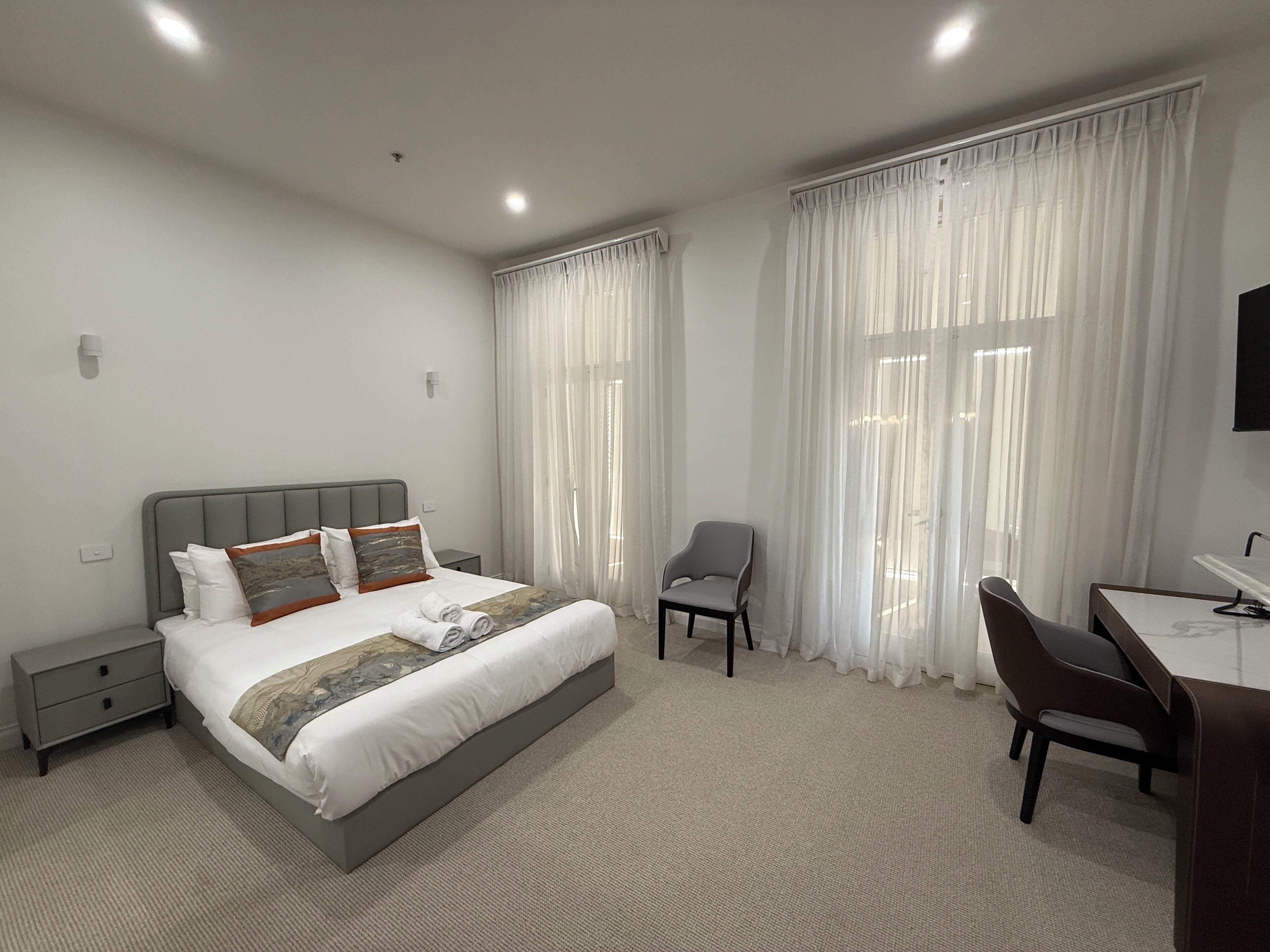 A modern hotel room with a large bed, a desk, and a chair.