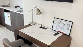 Un espacio de oficina moderno con un escritorio, una silla, una lámpara y un televisor de pantalla plana montado.