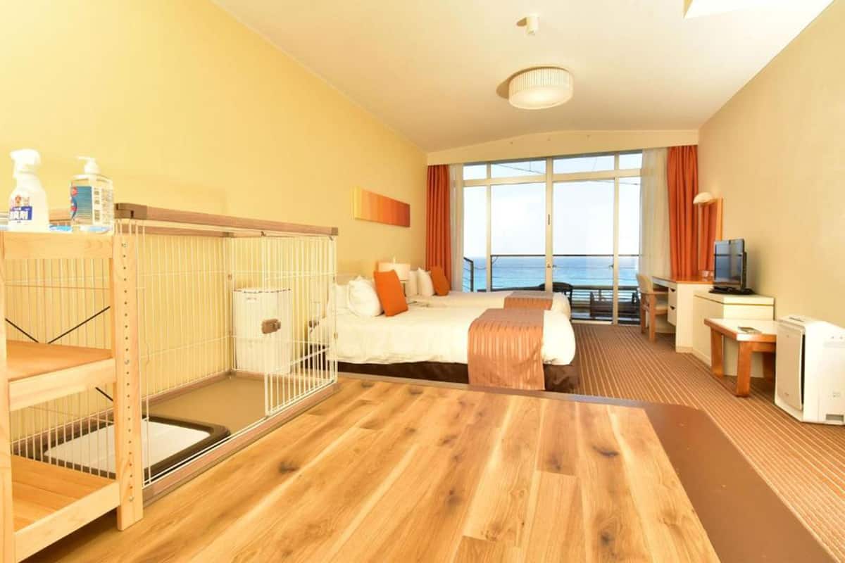 A hotel room with a bed, a desk, a television, and a view of the sea.