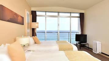 Habitación de hotel con dos camas, televisión, calefacción y un ventanal con vistas al mar.