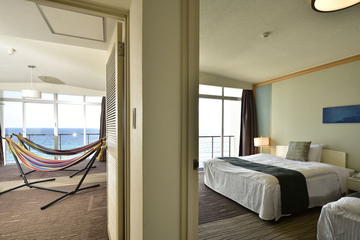 A hotel room with a large bed, a bedside table, a nightstand, a lamp, and a view of the ocean.