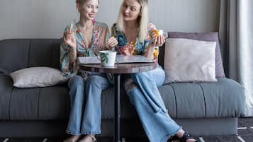 Dos personas sentadas en un sofá gris con una mesita redonda entre ellas, sosteniendo una taza y un vaso.