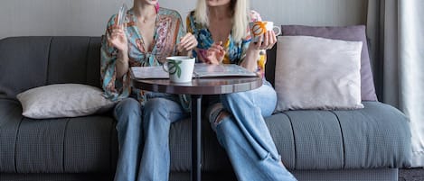 Two people sitting on a grey sofa with a small round table between them, holding a mug and a glass.