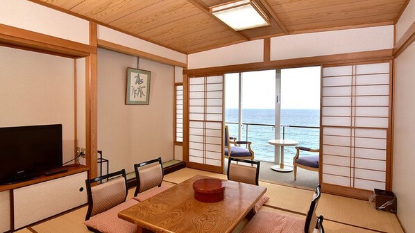 A traditional Japanese-style room with tatami flooring, a wooden table, and a television. It features a sliding shoji screen door leading to a balcony with a view of the sea. - Shimoda Prince Hotel (Shimoda)