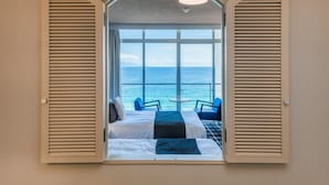 Een kamer met twee bedden, uitzicht op zee en een balkon met stoelen.