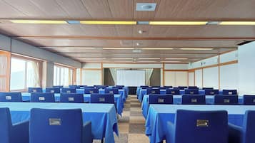 Un salón de conferencias con filas de mesas y sillas, paneles de techo de madera y ventanas amplias.