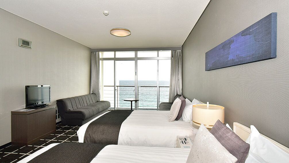 A hotel room with two beds, a sofa, a TV, and a view of the sea.