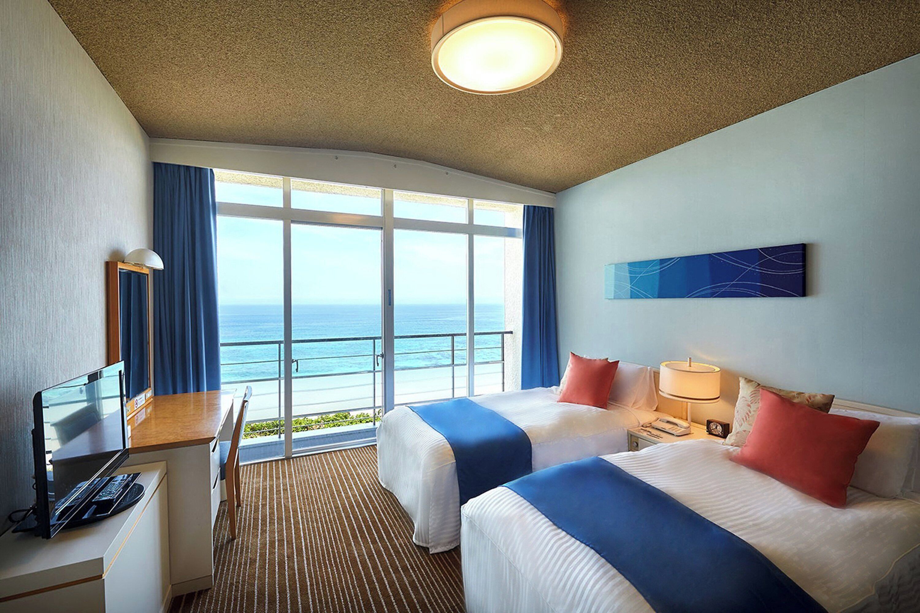 Ett hotellrum med två sängar, ett skrivbord med en dator, en telefon och ett fönster med utsikt över havet.