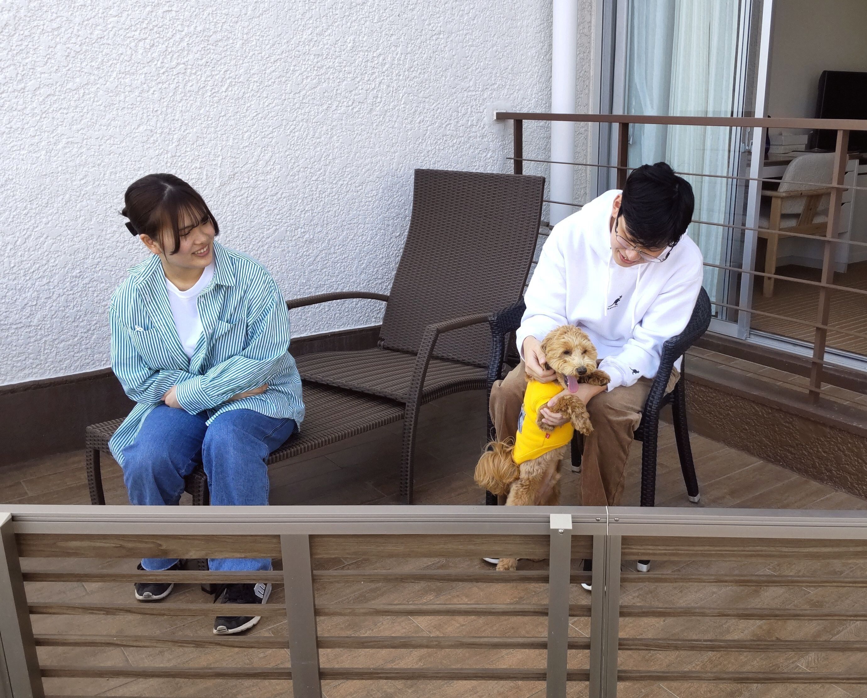 Two people sitting on wicker chairs on a balcony with a tiled floor.