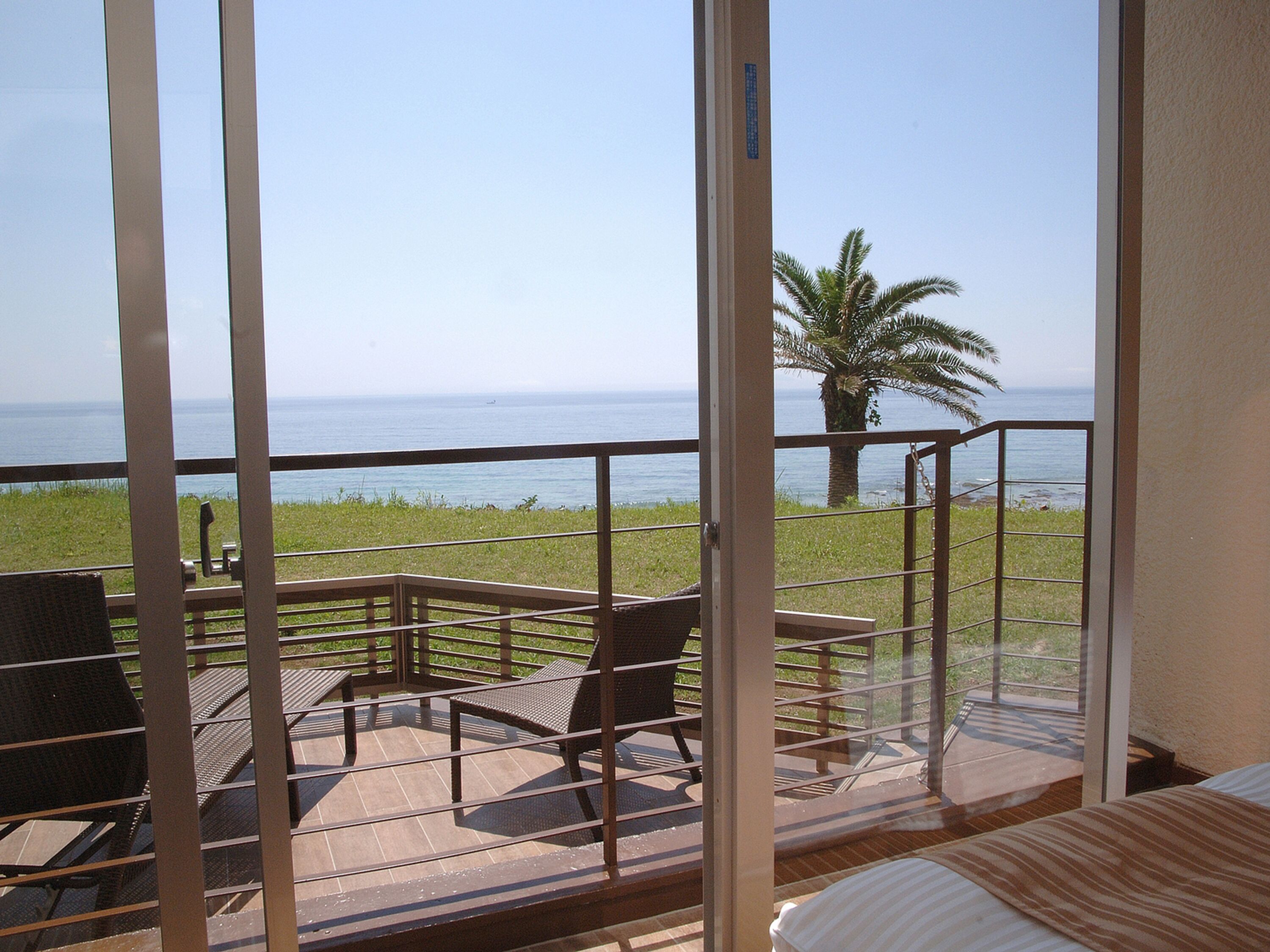 A balcony with a view of the ocean, equipped with wicker chairs and a table.
