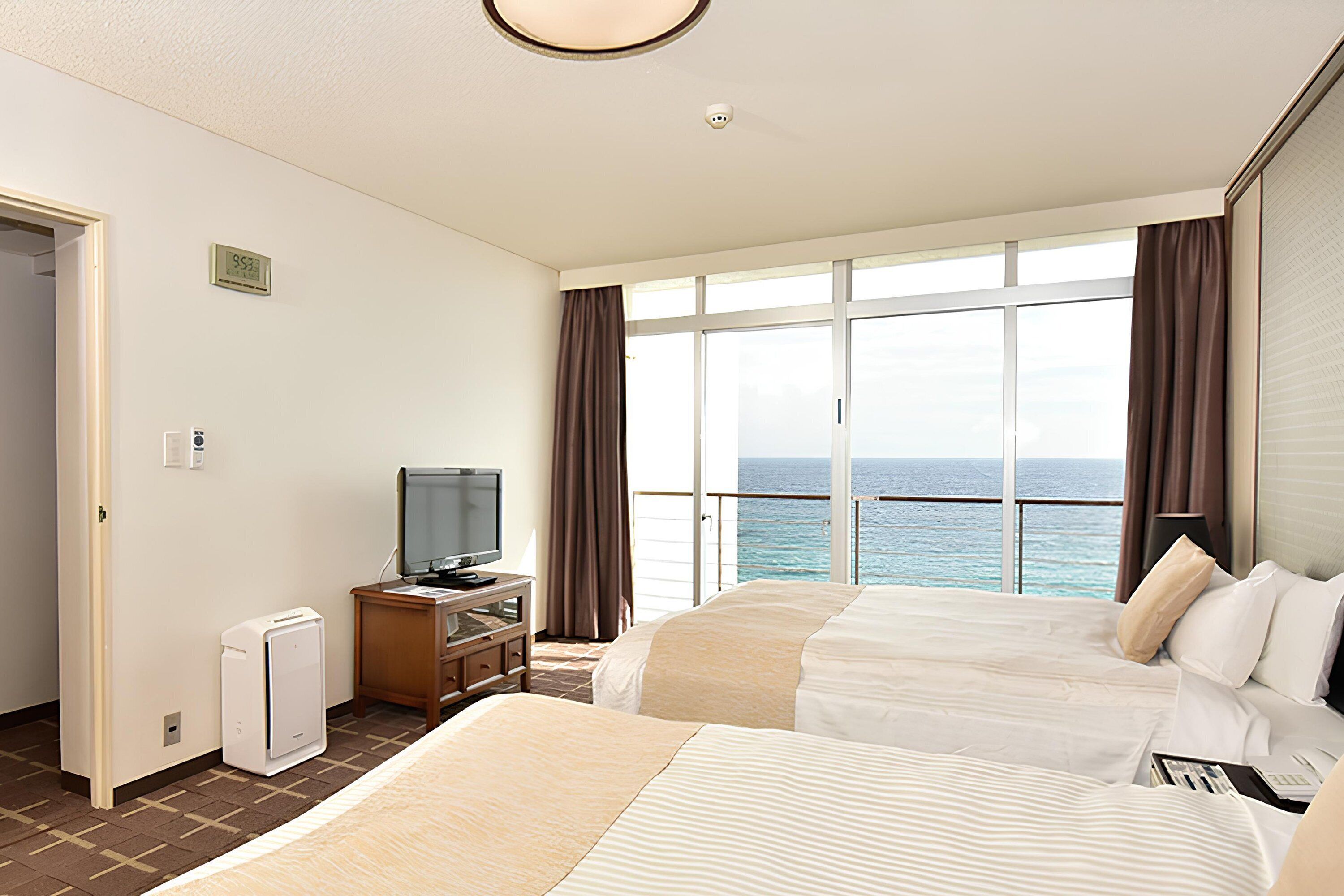 Une chambre d’hôtel avec deux lits, une télévision, un petit bureau et une vue sur la mer.