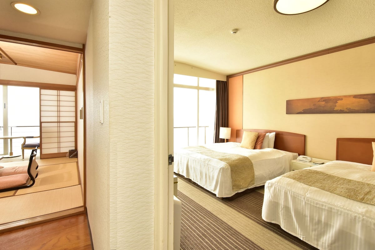 A hotel room with two beds, a large window, and a traditional Japanese sliding door.