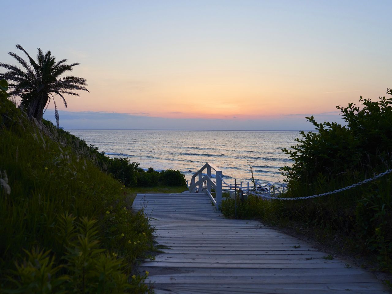 A wooden boardwalk leading to a bridge over a body of water at sunset.