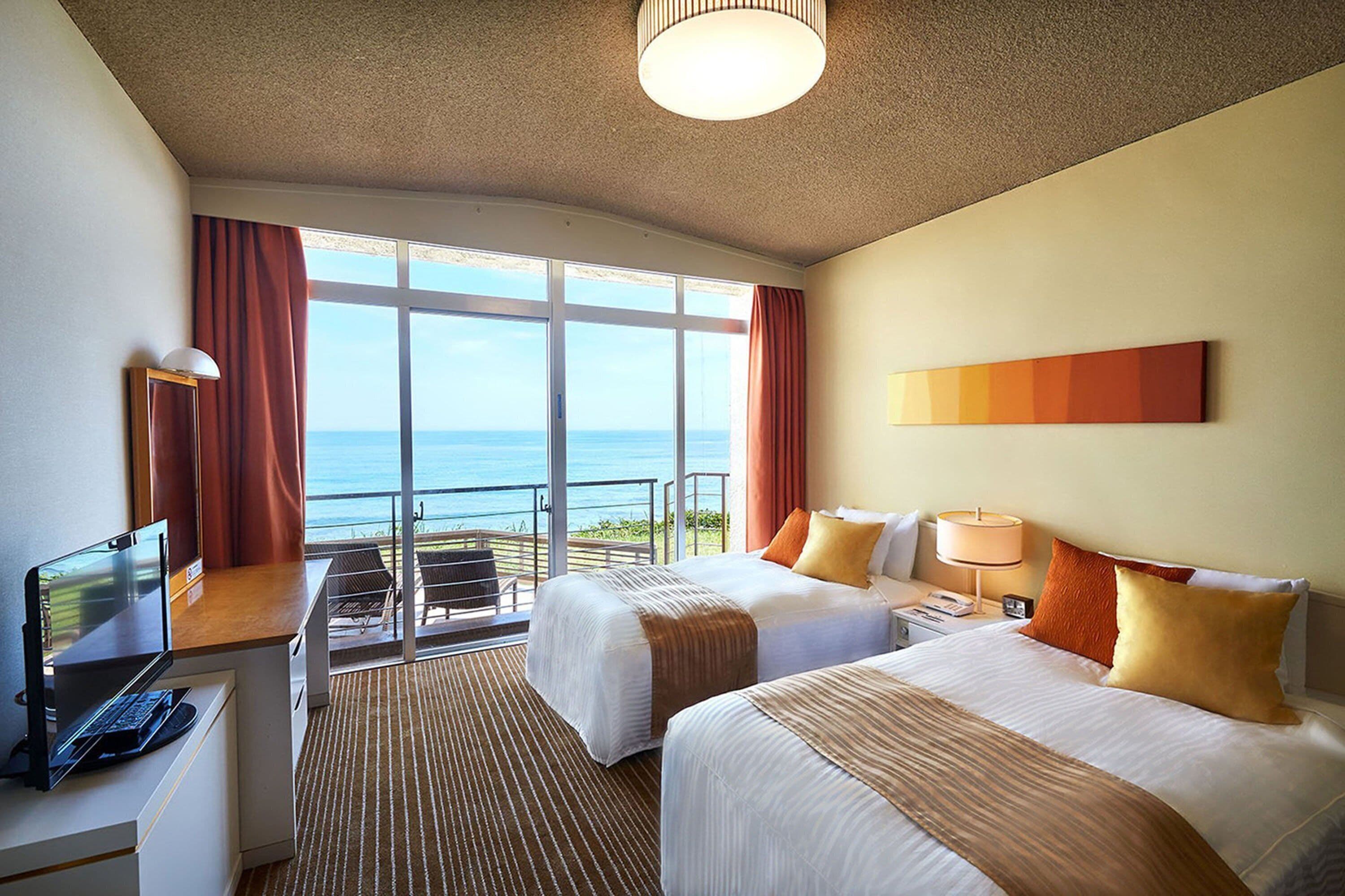 A hotel room with two beds, a desk with a computer, and a view of the ocean.