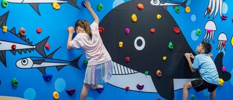 A climbing wall with colorful handholds and a large whale illustration.