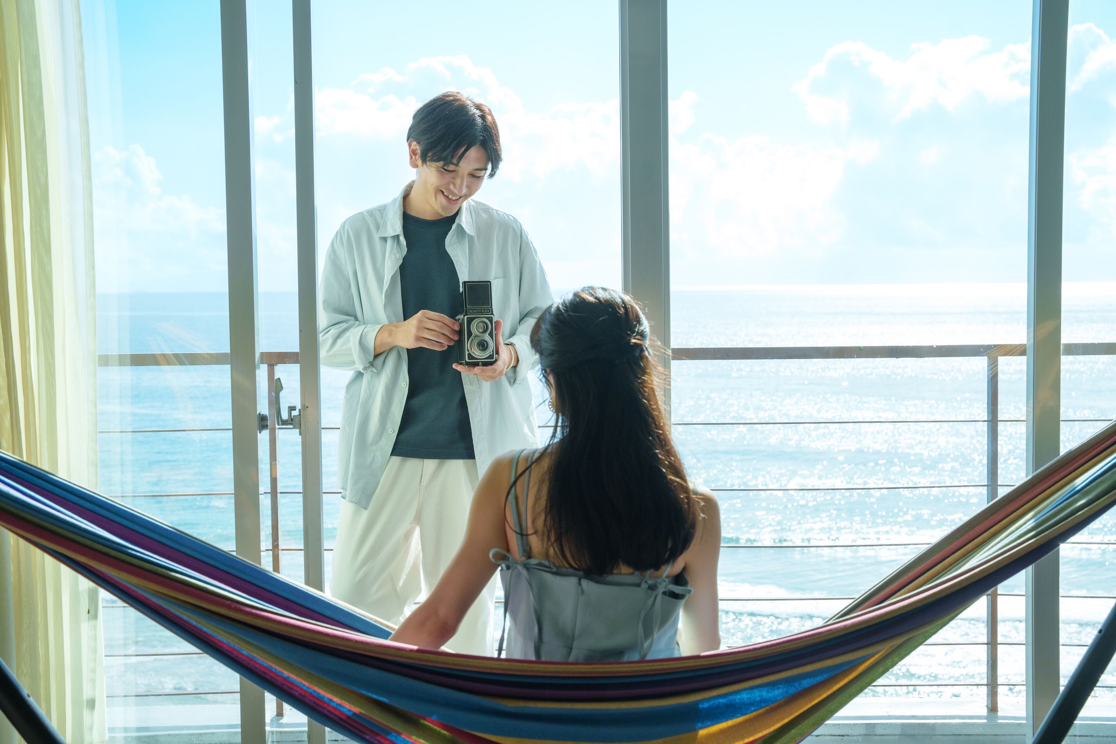 A balcony with a view of the sea, a hammock, and a person holding a camera.