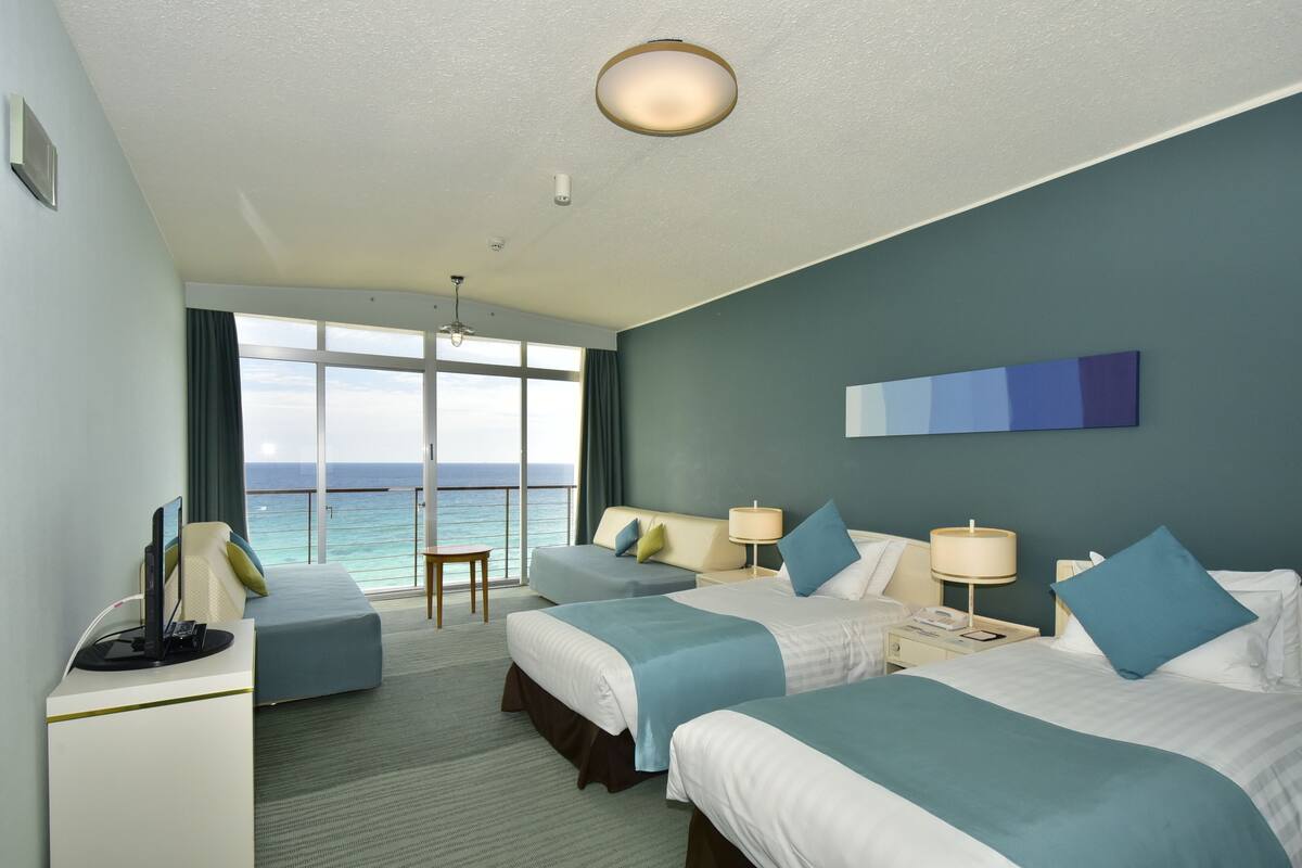A hotel room with two beds, a desk, a chair, and a view of the ocean.