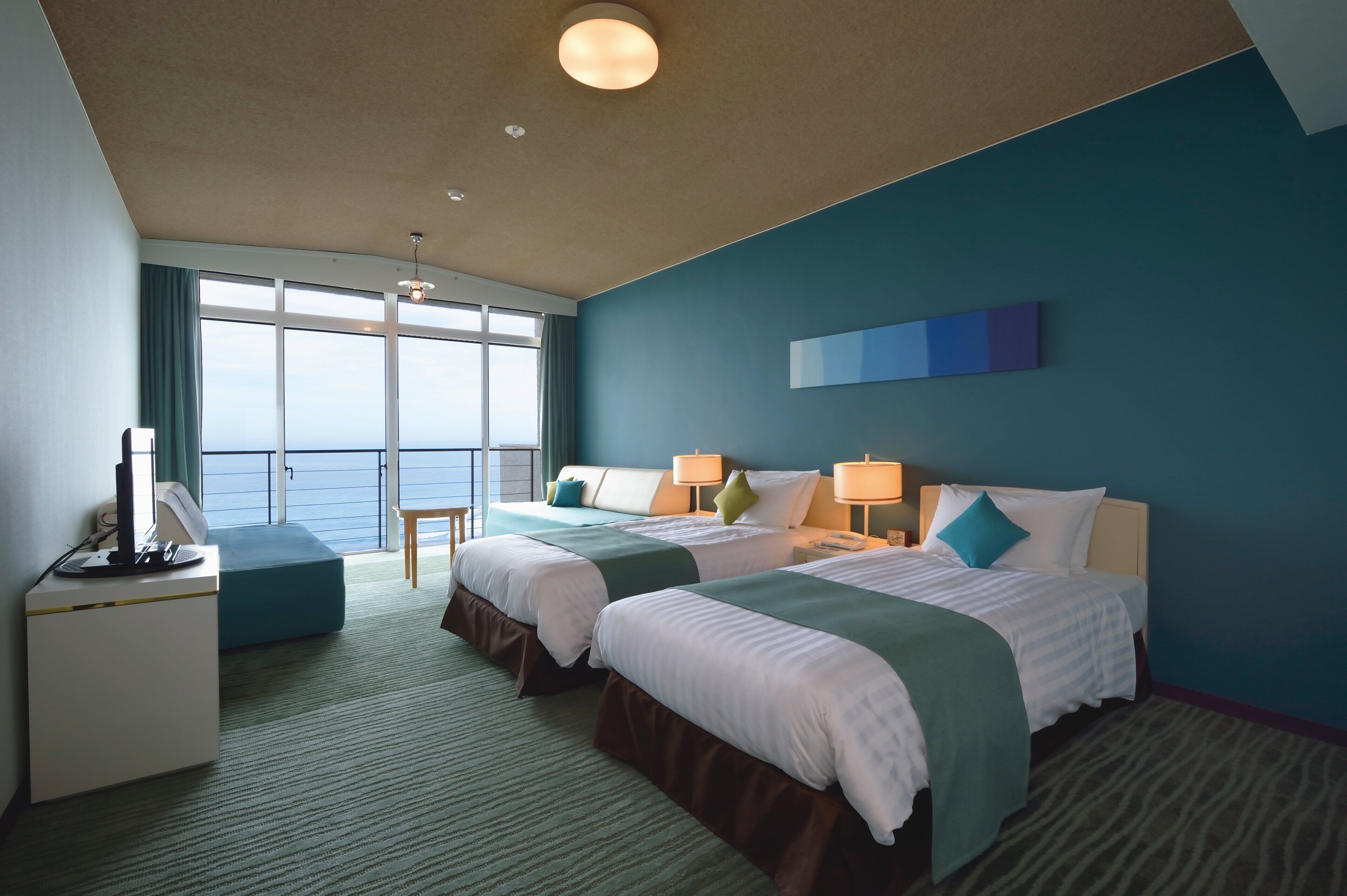 Een hotelkamer met twee bedden, een bureau en uitzicht op zee.