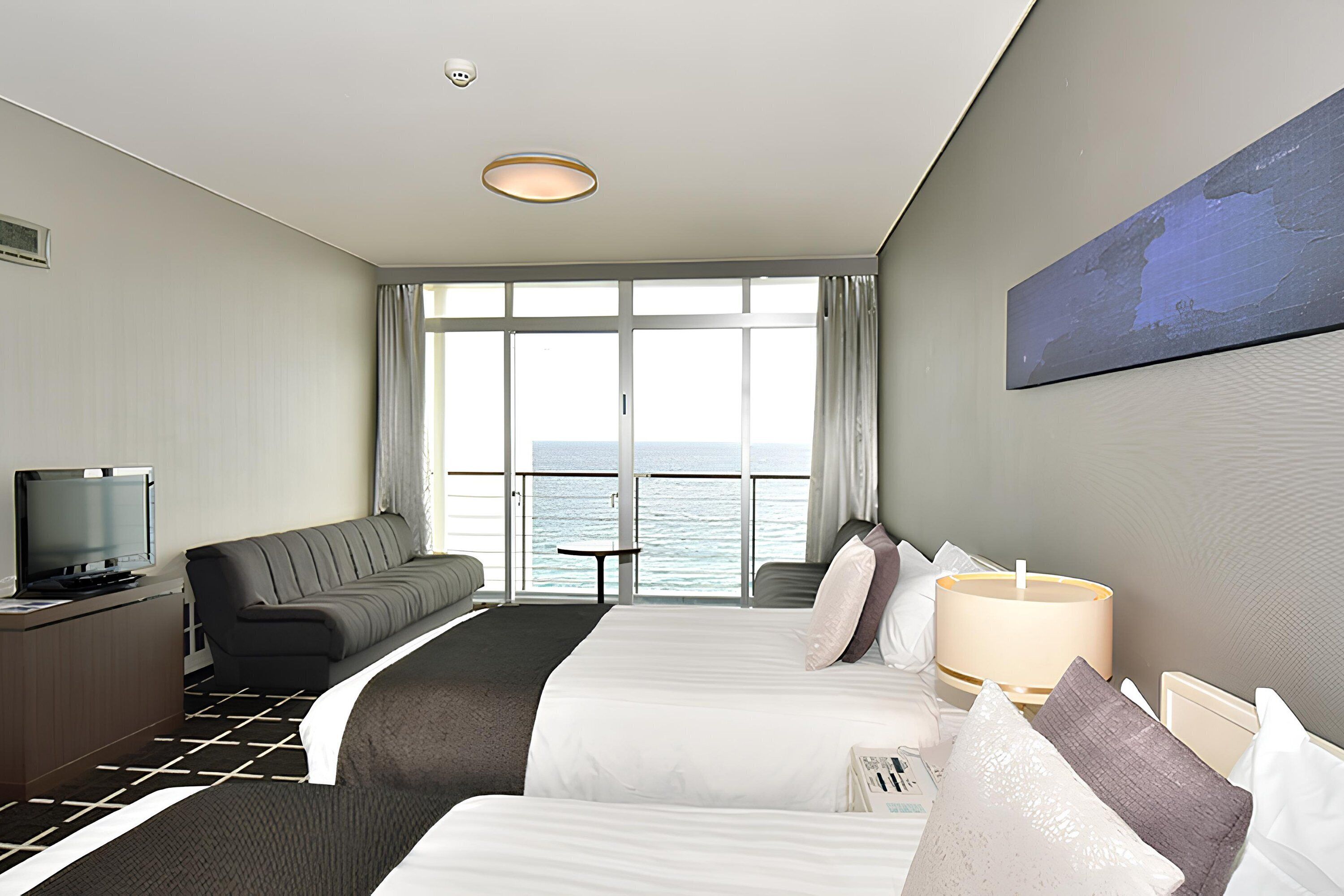 Habitación de hotel con dos camas, televisión, sofá, mesa y vista al mar.
